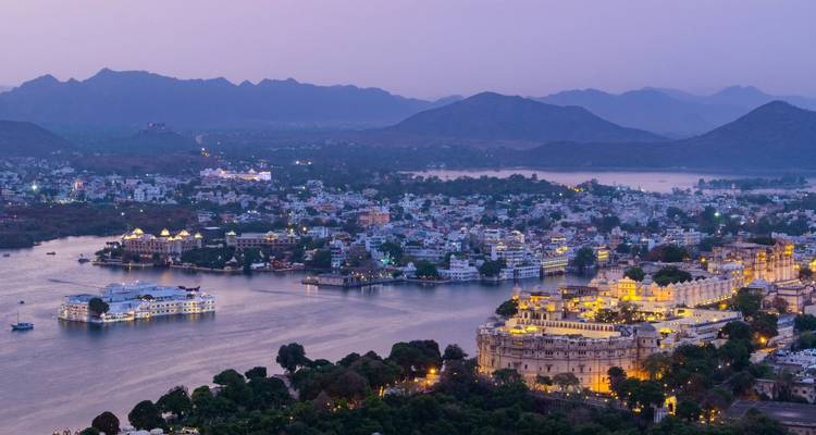 Twilight aerial panorama of Udaipur’s lakes, palaces and surrounding Aravalli hills glowing with lights.
