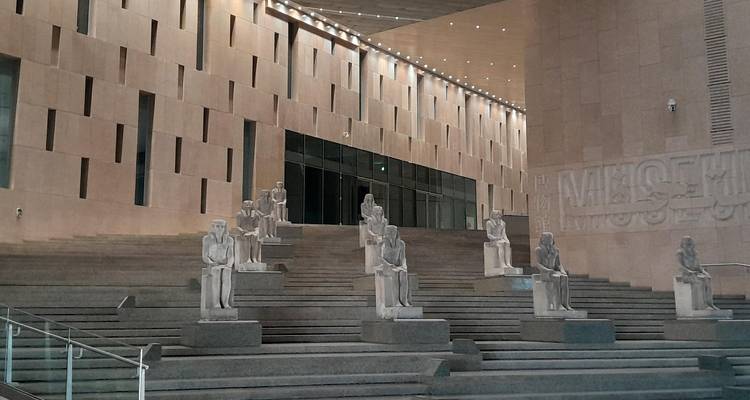 Symmetrical staircase lined with seated ancient statues inside the museum’s stone hall.