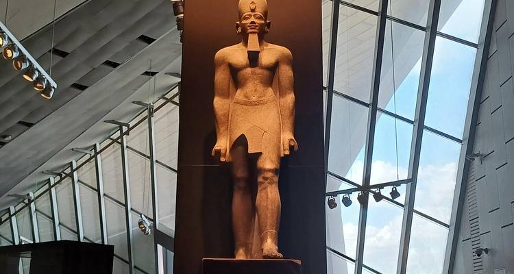 Tall granite statue of an Egyptian pharaoh displayed against lofty glass walls.
