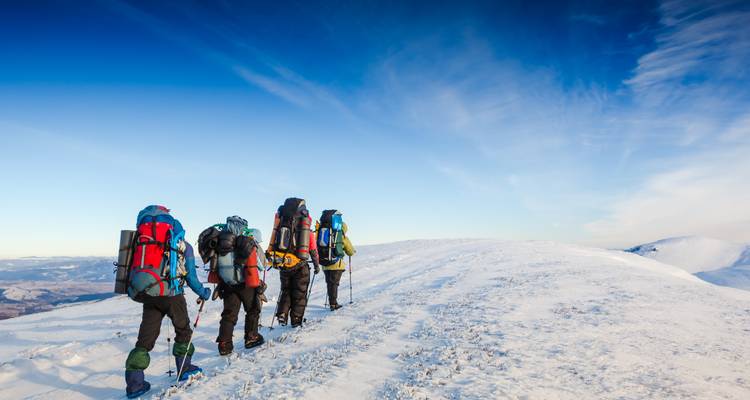 Group of trekkers with backpacks walking along a snowy ridge toward blue sky