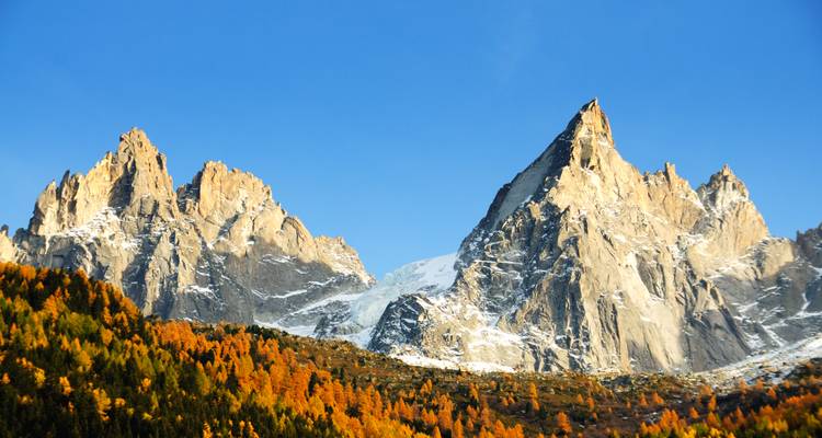 Sharp rocky mountain peaks dusted with snow rising above autumn coloured forest