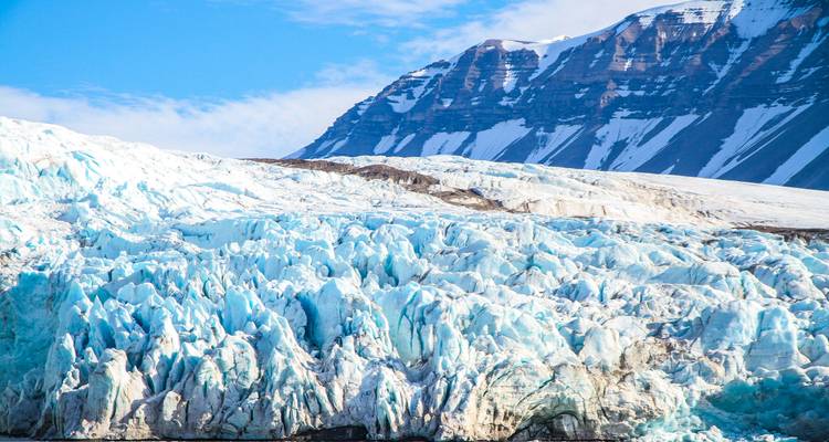Massive jagged blue ice face of a glacier beneath a snow-striped mountain