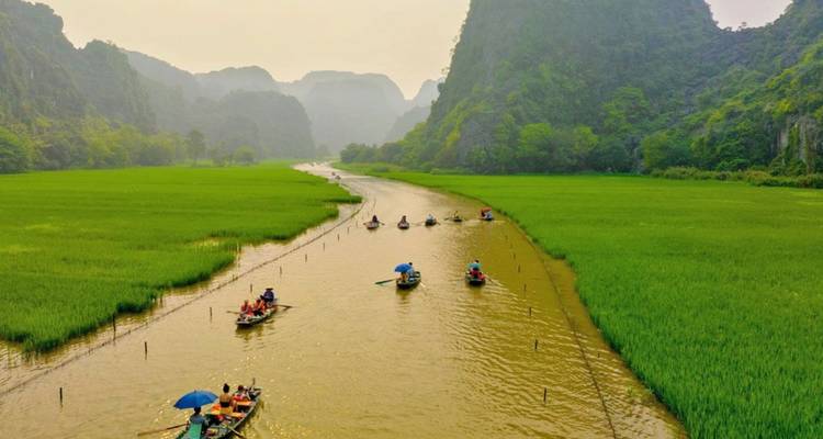 Small sampan boats glide along a winding river through emerald rice fields and limestone karsts at Tam Coc.