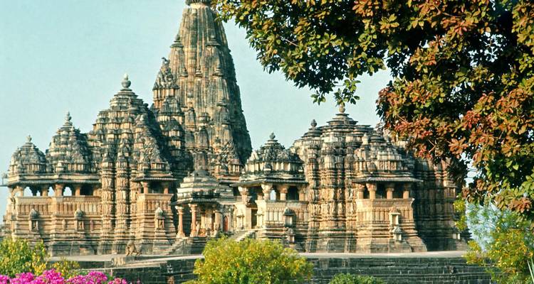Aufwändig geschnitzte Sandsteintempel von Khajuraho, eingerahmt von blühenden Bäumen