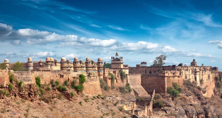 Die langen Verteidigungsmauern und Kuppelpaläste der Gwalior-Festung erstrecken sich über einen felsigen Höhenzug unter blauem Himmel