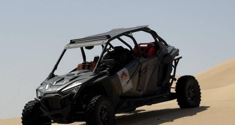 Black off-road buggy parked diagonally on a steep sand dune beneath a clear blue sky