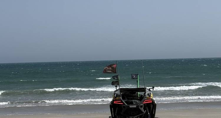 Rear view of a flag-topped buggy parked on a quiet sandy beach facing turquoise ocean waves