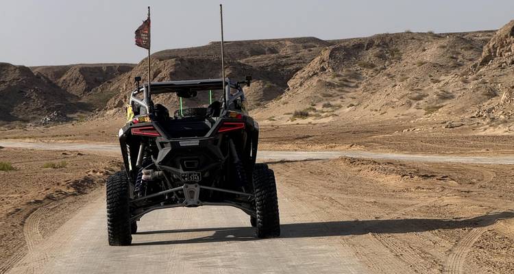 Off-road buggy driving on a dusty desert track bordered by rocky hills under bright daylight