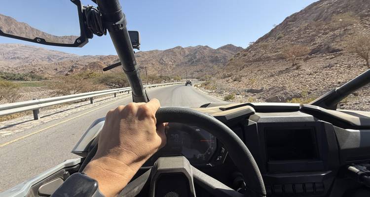 First-person view from inside a buggy steering down a winding mountain road with rocky peaks ahead