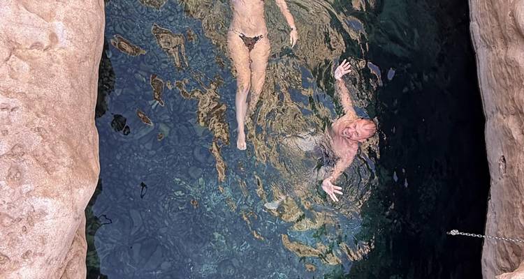 Top-down view of two swimmers floating in a narrow turquoise rock pool surrounded by canyon walls