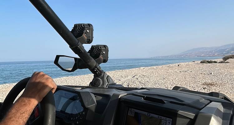 Driver’s perspective of a buggy cruising along a pebbly shoreline with calm blue sea to the left