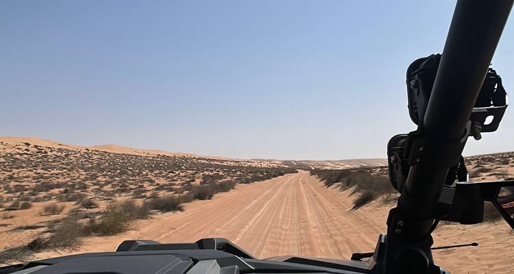 View over buggy dashboard heading down a long sandy desert track under a hazy blue sky