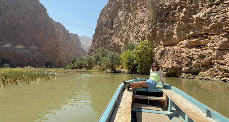 Woman relaxing on the bow of a small boat gliding through a narrow palm-lined canyon river