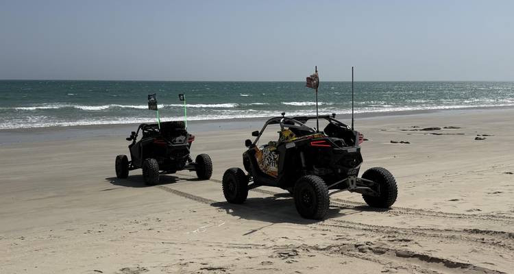 Two off-road buggies parked on a wide empty beach beside gentle ocean surf