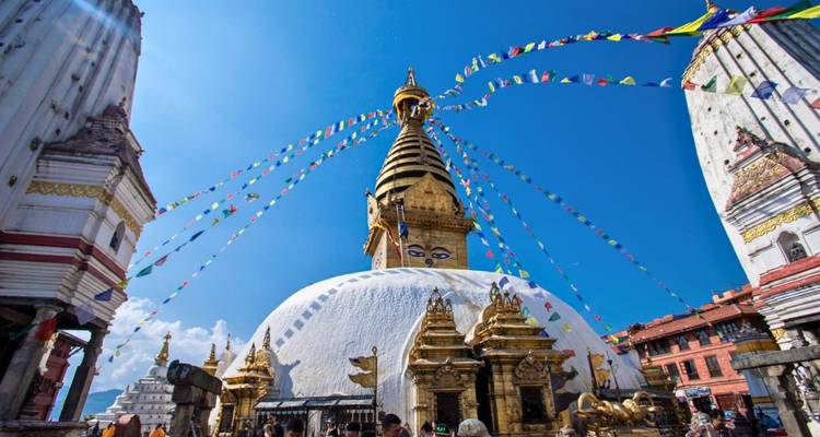 The white dome of Swayambhunath Stupa rises beneath prayer flags against a vibrant blue Kathmandu sky.