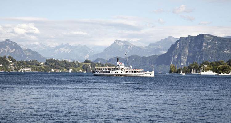 Un ancien bateau à aubes blanc navigue sur le lac de Lucerne avec des crêtes alpines escarpées en arrière-plan.