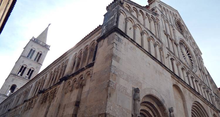 Low-angle view of a Romanesque cathedral corner and adjacent bell tower against a pale sky.