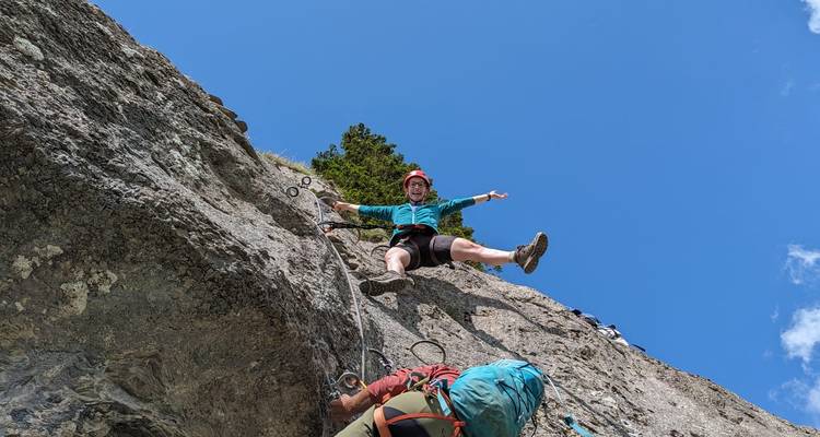 Kletterer in der Luft auf einer Via-Ferrata-Route vor einem hellen blauen Alpenhimmel.