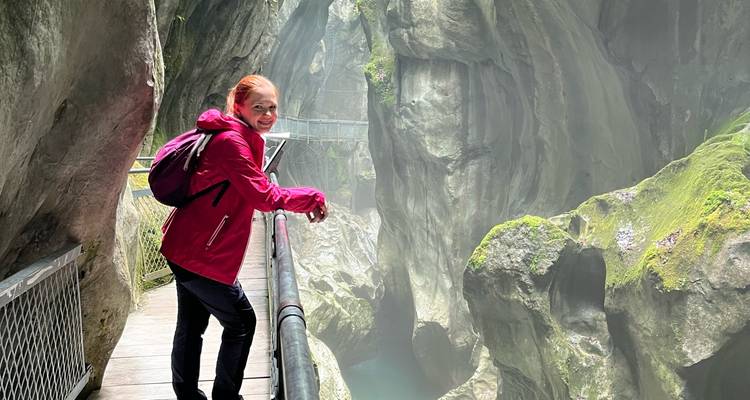 Wanderer in einer roten Jacke auf einem Holzweg in einer nebligen Kalksteinschlucht.