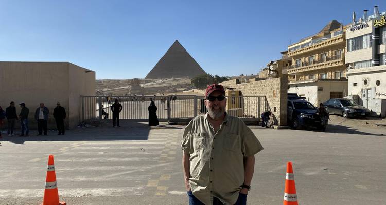 Vergelijkbare scène van een bezoeker die op een weg staat met een piramide in de verte en stedelijke gebouwen in de buurt.