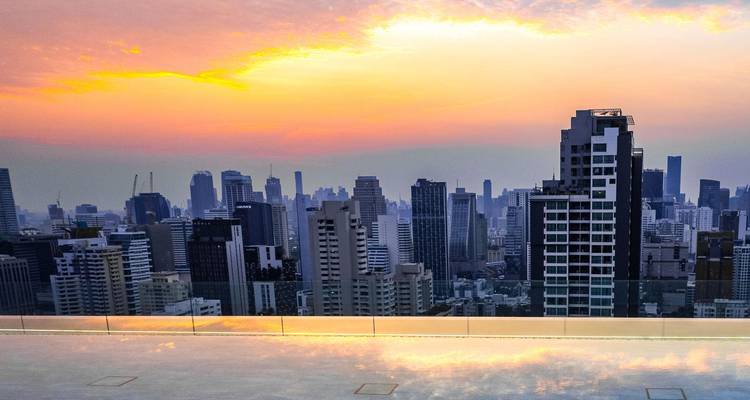 Le skyline de Bangkok brille sous un coucher de soleil coloré depuis un toit élevé.
