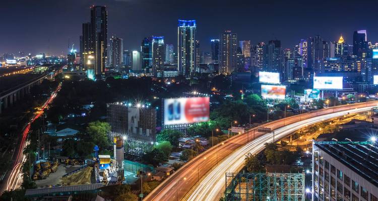 Vue nocturne de Bangkok avec des traînées lumineuses sur une autoroute surélevée très fréquentée.