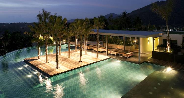 Piscine à débordement élégante avec îlot planté de palmiers illuminé après le crépuscule.
