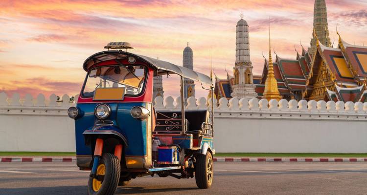 Un tuk-tuk classique garé devant le Grand Palais de Bangkok au lever du soleil coloré.