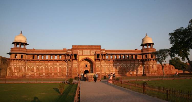 Long red-sandstone fort entrance in Agra lit by warm evening light with visitors strolling along the path.