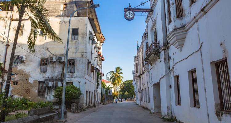 Calle estrecha en Stone Town bordeada de edificios coloniales blancos desgastados por el tiempo y un letrero de reloj colgante vintage