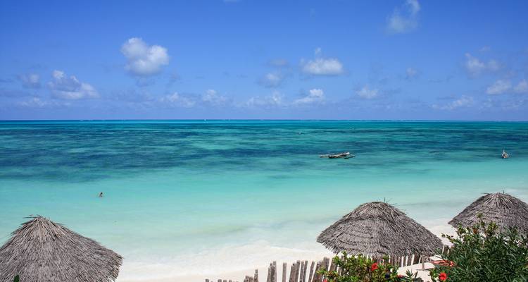 Laguna turquesa vibrante y arrecife vistos sobre sombrillas de playa con techo de paja y arena coralina