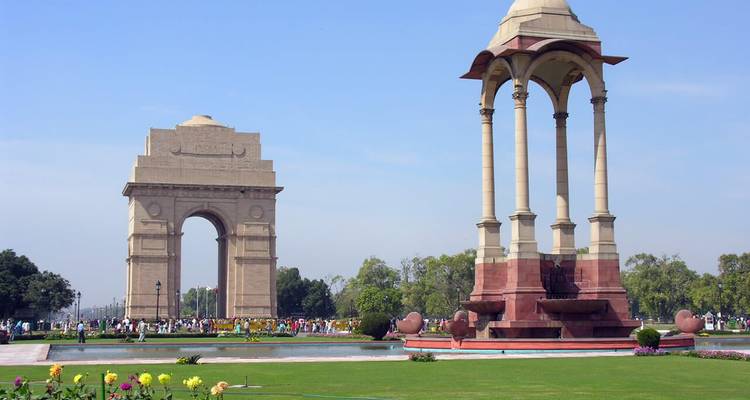 Les jardins luxuriants et les parterres de fleurs colorés encadrent l'arche de pierre de l'India Gate et son dais sous un ciel dégagé.