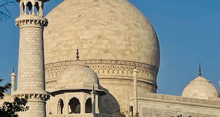 Gros plan du dôme en ivoire du Taj Mahal et du minaret illuminés contre un ciel bleu profond.