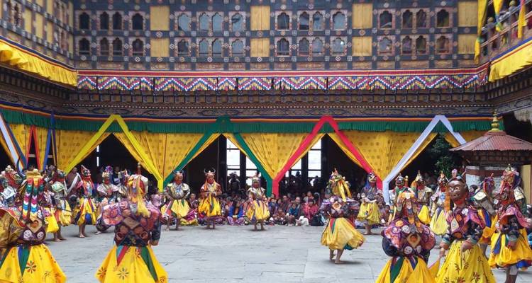 Masked dancers in bright yellow costumes perform a traditional festival inside an ornately painted courtyard.