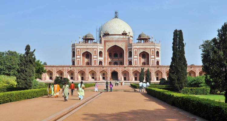Visitors approach the symmetrical red-sandstone Humayun's Tomb surrounded by manicured gardens and cypress trees.