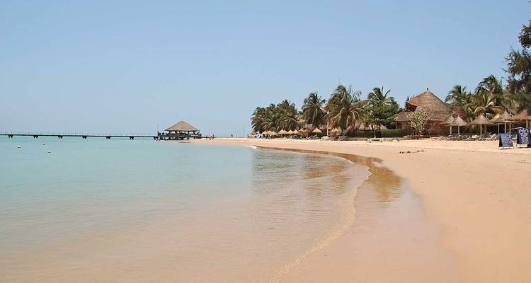 Peaceful sandy beach with calm turquoise water, palm trees and a distant pier