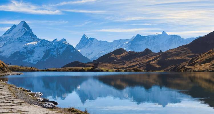 Crystal alpine lake reflecting jagged snow-capped peaks under blue sky