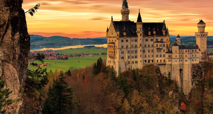 Fairytale hilltop castle with tall turrets set against glowing sunset sky