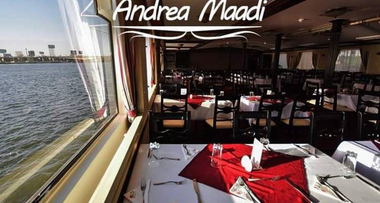 Salle à manger intérieure du bateau Andrea Maadi avec des tables soigneusement dressées à côté de grandes fenêtres donnant sur la rivière.