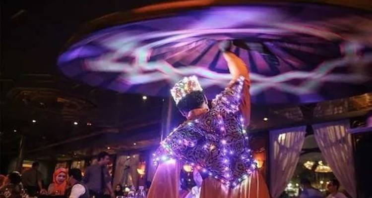 Un danseur de tanoura tourbillonnant se fait tournoyer sous des lumières violettes éclatantes, laissant des traînées de mouvement de la jupe illuminée.