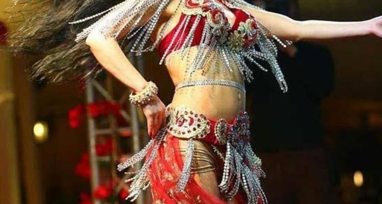 Une danseuse du ventre vêtue d'un costume rouge orné de paillettes se produit en plein mouvement avec ses cheveux qui ondulent et ses perles scintillantes.