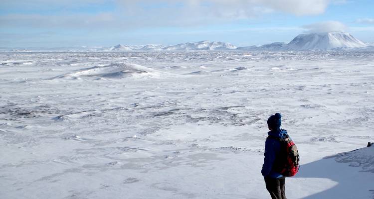 Person in blauem Jackett, die über eine endlose schneebedeckte Vulkanebene auf entfernte Vulkankegel blickt