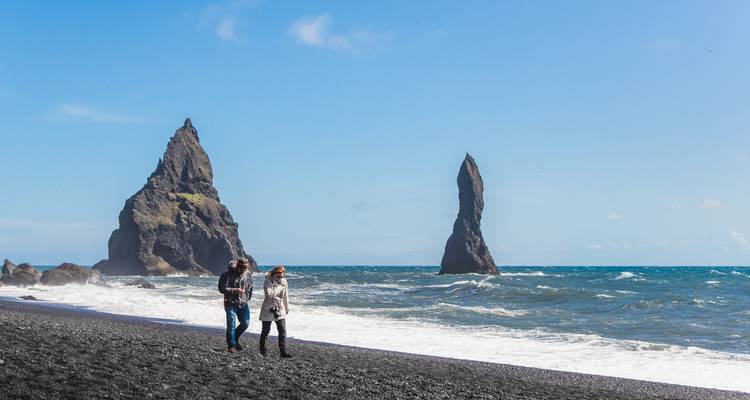 Stel dat langs het zwarte zandstrand van Reynisfjara loopt met dramatische basalten zeestapels en kolkende golven.