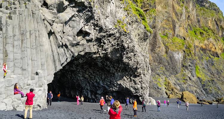 Toeristen die de basaltkolom-grot en zwart zand van Reynisfjara verkennen onder helder licht.