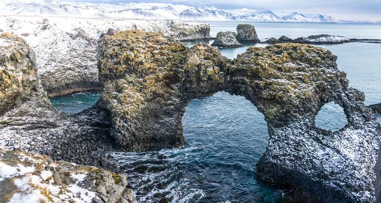 Sneeuwbestoven Gatklettur zeepoort en ruige kustlijn met turquoise water eronder.