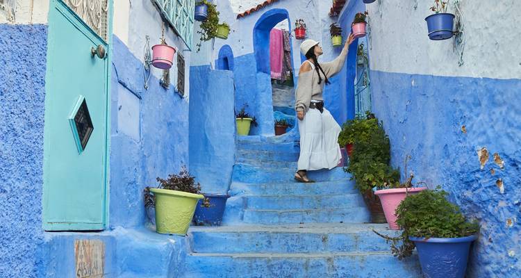 A woman in white explores the iconic blue-washed steps decorated with colorful pots in Chefchaouen.
