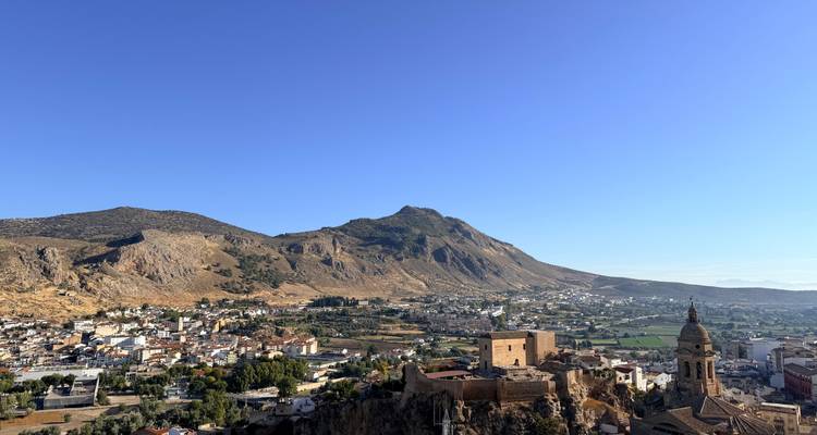 Panoramablick auf eine spanische Stadt und ein zerklüftetes Gebirge, das sich schroff hinter terrakottafarbenen Dächern erhebt.