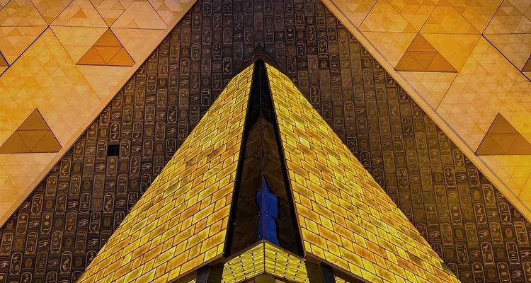 Façade extérieure du musée illuminée la nuit présentant un design de pyramide dorée
