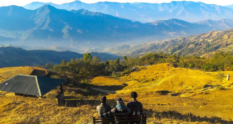 Three friends sitting on a bench admiring golden terraced hills and distant Himalayan ridges.