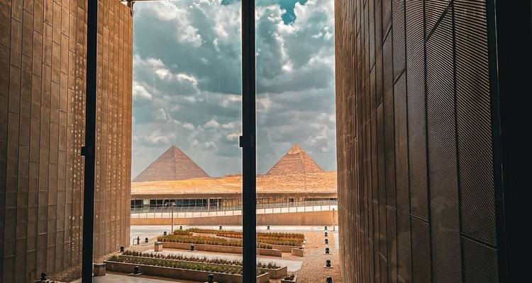 Vue encadrée à travers la porte du musée révélant deux pyramides de Giza sous des nuages dramatiques.
